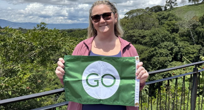 Lauren Schexnider, a first-generation college student and MBA candidate, is pictured in Costa Rica holding a green flag with the word "GO."